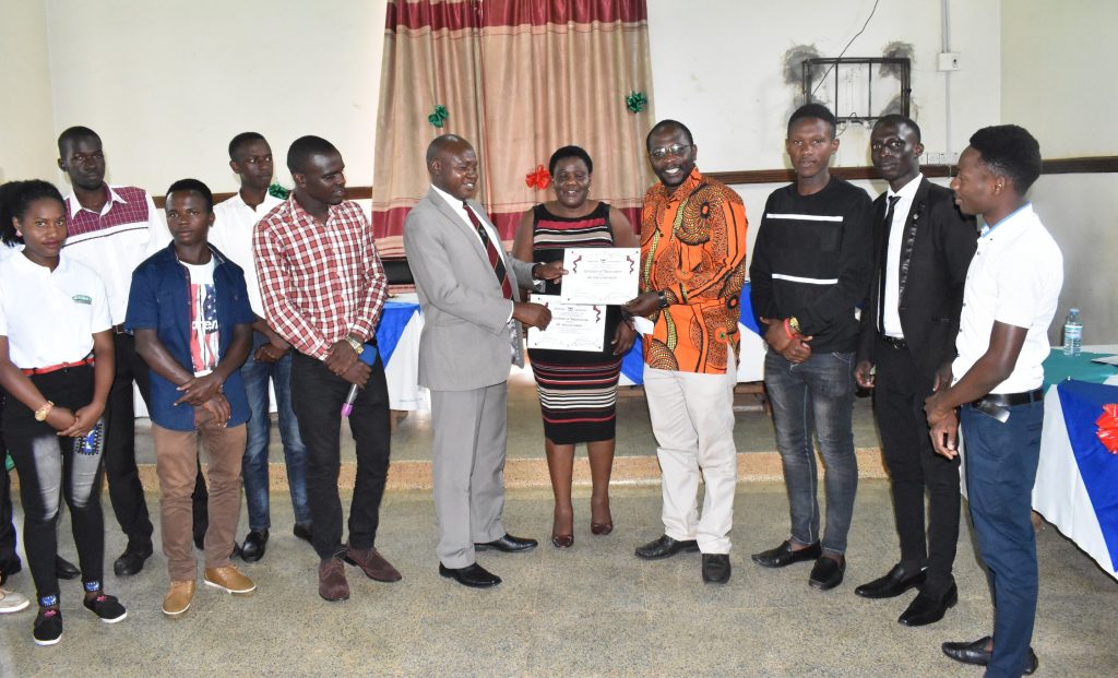  - Dr. Owinyi David in a suit presents a certificate of appreciation from the students to the Recess term coordinators Dr. Sarah Akello and Mr. Anthony Mwijje
